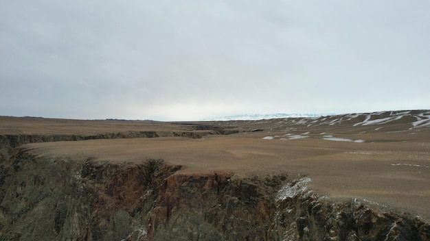 A large crack in the ground overlooking the snowy hills. Grey sky covered with clouds.