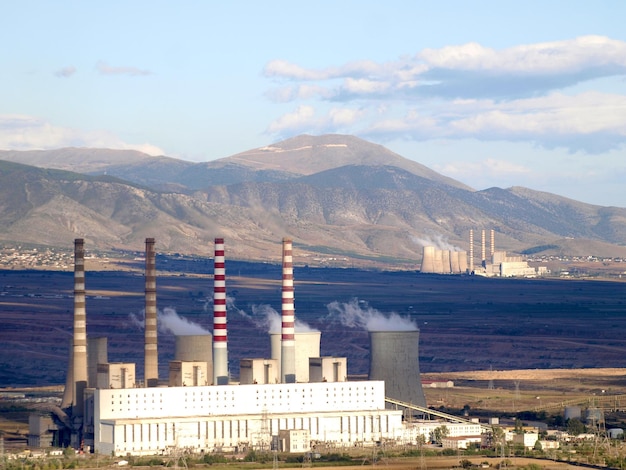 A large factory with smoke stacks and mountains in the background