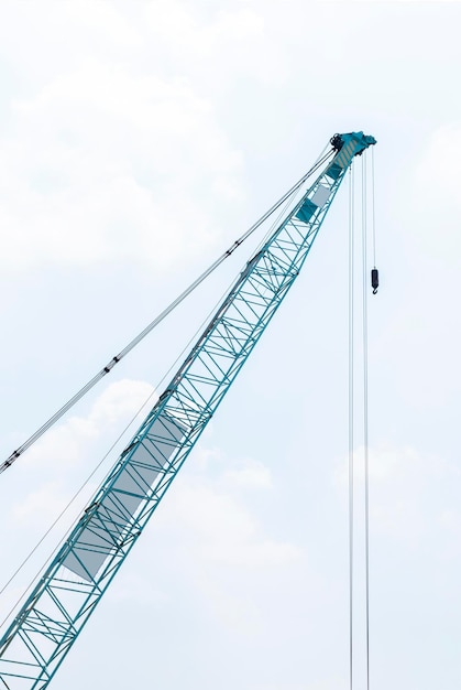 Large green crane boom with hooks with sky background