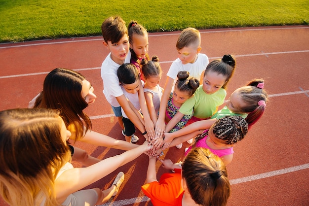 A large group of children boys and girls stand together in a circle and fold their hands tuning up and raising team spirit before the game at the stadium during sunset A healthy lifestyle