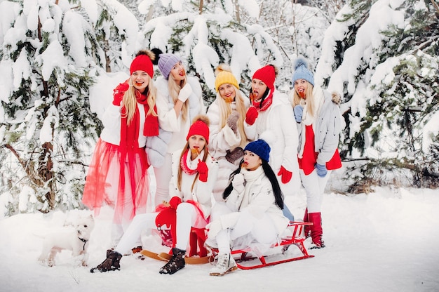 A large group of girls with lollipops in their hands stands in the winter forest.Girls in red and white clothes with candy in a snow-covered forest.