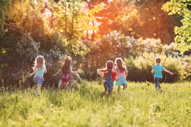 Large group of kids, friends boys and girls running in the park on sunny summer day in casual clothes .