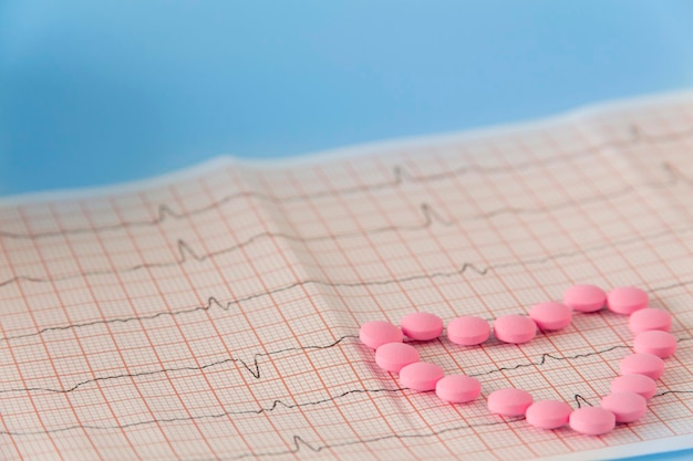 A large handful of pink pills lie in the form of a heart on an electrocardiogram on a blue background The concept of a healthy lifestyle and timely medical examination