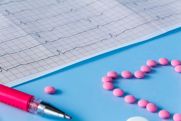 A large handful of pink pills lie in the form of a heart on an electrocardiogram on a blue background The concept of a healthy lifestyle and timely medical examination