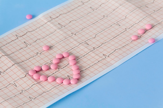 A large handful of pink pills lie in the form of a heart on an electrocardiogram on a blue background The concept of a healthy lifestyle and timely medical examination