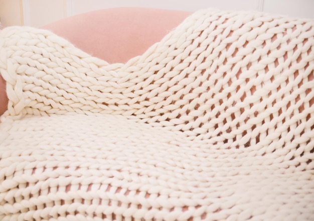 Large handmade merino wool blanket, super thick yarn, fashionable concept. Close-up of a knitted blanket on the sofa. Coziness and comfort.