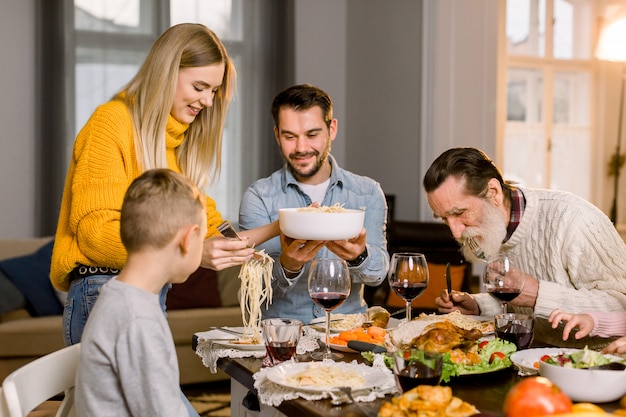 Large happy family enjoying time together having tasty dinner, vegetable salad, pasta, turkey