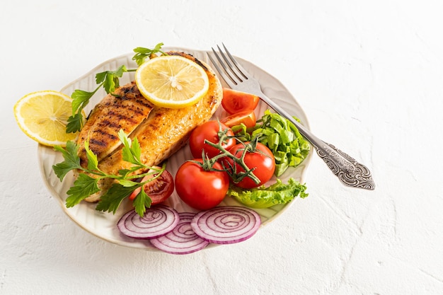 A large juicy piece of grilled chicken chicken breast fresh vegetables on a white ceramic plate white background a copy of the space menu