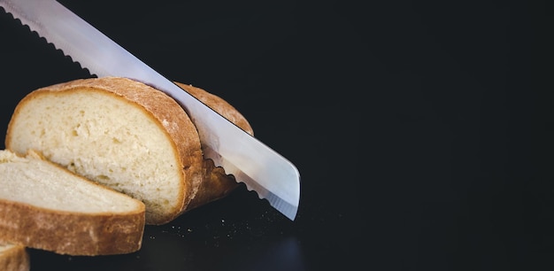 A large knife cuts thin pieces of white bread from a rectangular loaf