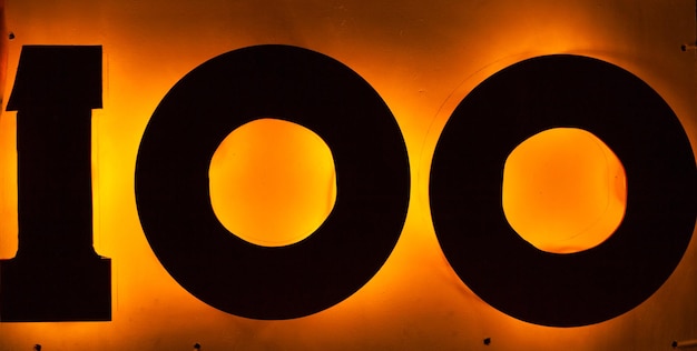 A large number one hundred silhouetted against a yellow illuminated surface closeup