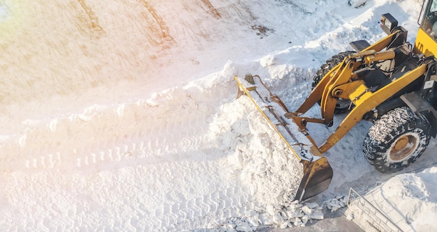 A large orange tractor removes snow from the road and clears the sidewalk.