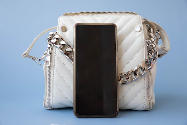 A large phone with a black screen stands next to a small white women's bag