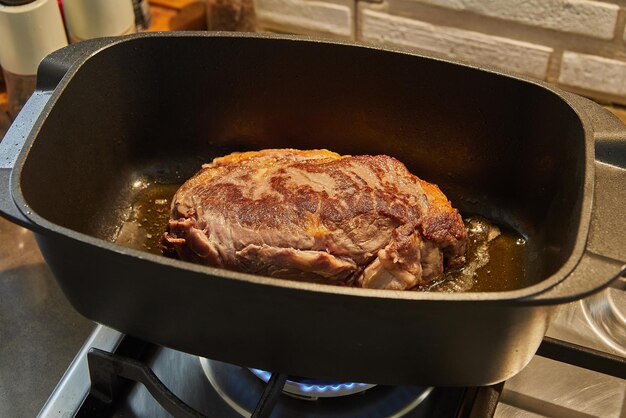 Large piece of beef is fried in special cauldron on gas stove.