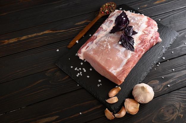 A large piece of pork loin with basil on a rustic dark background