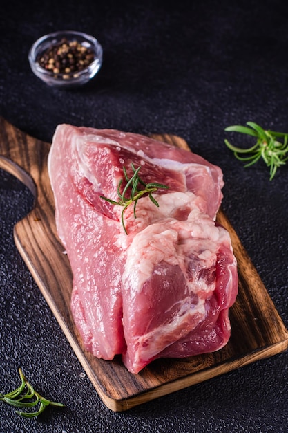 Large piece of pork rosemary and salt on a cutting board on a black background Vertical view