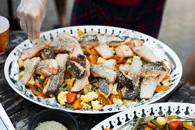 a large plate of grilled fish dish with vegetables on a picnic