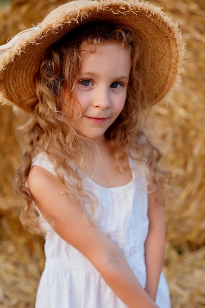 large portrait of a curly-haired girl in a straw hat on a hay background