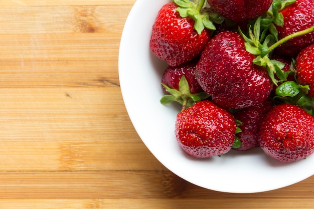 Large red strawberries lie in a white plate on a wooden surface