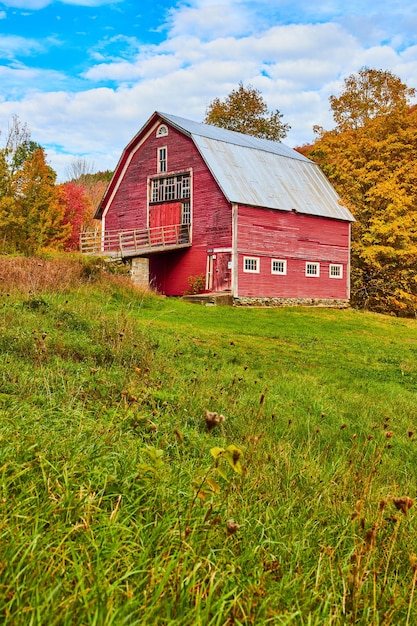 Large red vintage country barn in grassy fields with fall trees behind