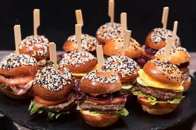 Large set of many hamburgers, cheeseburgers laid out on a table on a dark background. Seth fast food. Dark background, copy space.