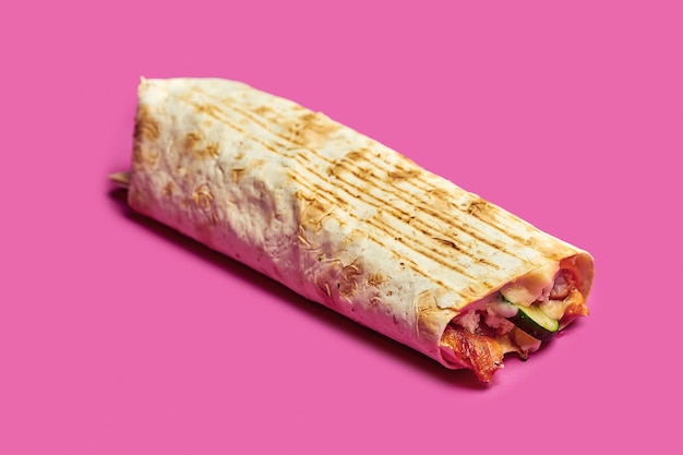 Large shawarma with chicken, vegetables and sauce on a pink background.