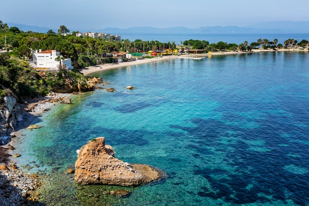 A large stone in the form of a heart in the turquoise blue sea and the green shore on a bright sunny day. Great view of the beautiful bay. Relax and tranquility. Postcard. Space for text.