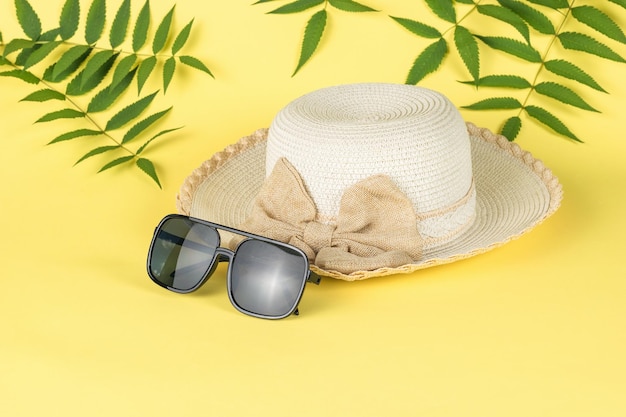 A large sun hat and sunglasses on a yellow background with palm leaves