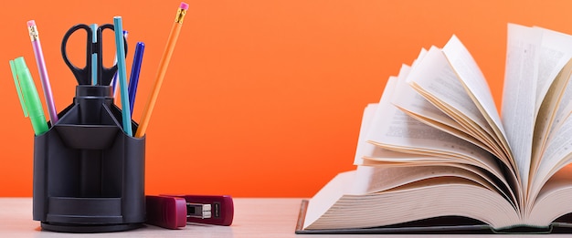 A large thick book with the pages spread out like a fan and a stand with pens and school supplies