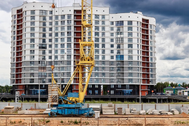 A large tower crane at a construction site against the backdrop of a modern monolithic house Modern housing construction industrial engineering Construction of mortgage housing