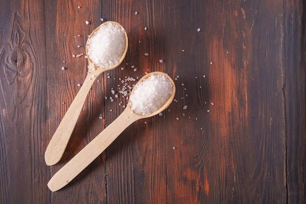 Large white crystal salt in spoons on a wooden background top view