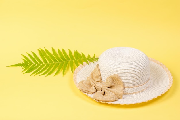 A large white hat and a palm leaf on a yellow background