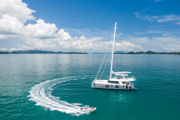 A large white sailing yacht and a motor boat with people.