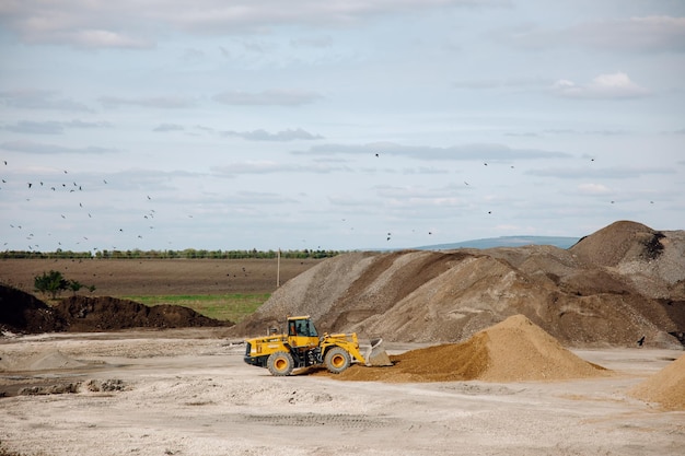 A large yellow bulldozer is in a field with a large pile of gravel.