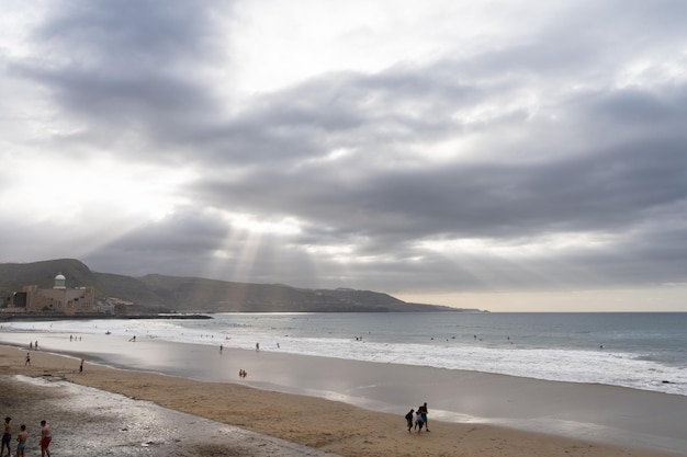 Las Palmas Spain March 30 2021 Sun rays piercing clouds over Las Canteras beach in Gran Canaria