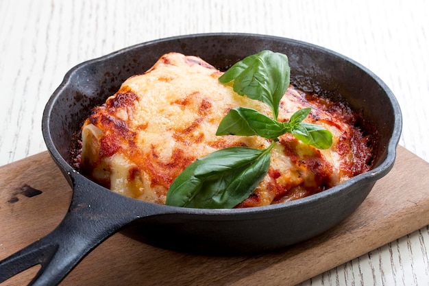 Lasagna in a cast iron pan on a wooden board Traditional Italian dish