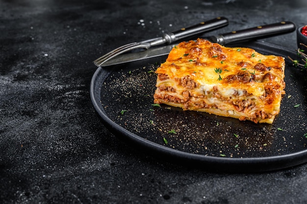 Lasagna with mince beef meat and tomato bolognese sauce on a plate. Black background. Top view. Copy space.