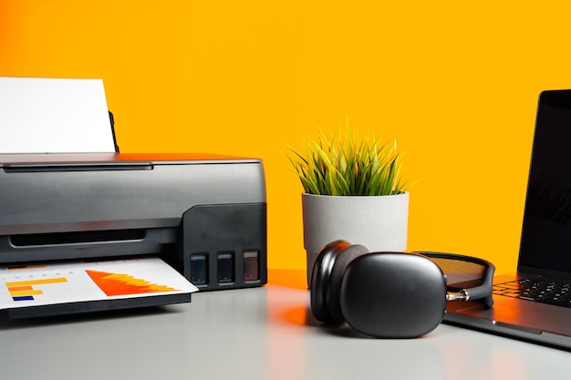 Laser printer and laptop on desk against yellow background