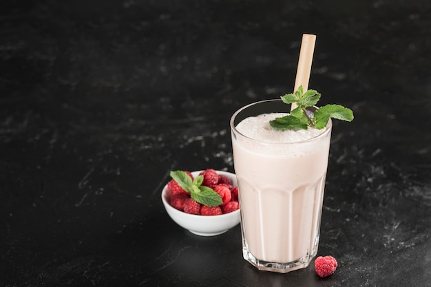 Lassi drink with raspberries in a glass with mint and a bamboo tube on a dark background. Horizontal orientation. Indian traditional refreshing drink.