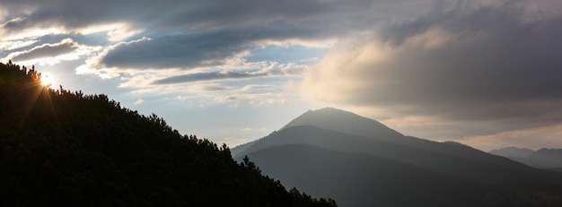 Last sun rays in evening sky with clouds above Syniak mountain. Summer sunset view from Homiak mountain, Gorgany, Carpathian, Ukraine.