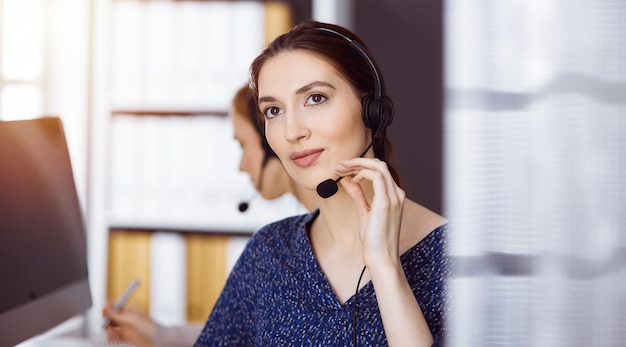 Latin american businesswoman talking by headset in office. Call center and diverse people group in business.