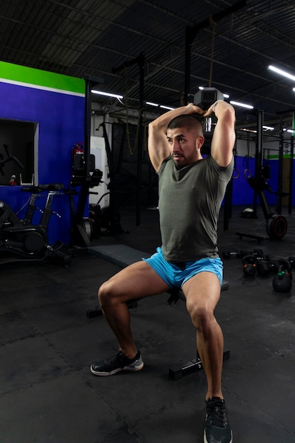 Latin athlete doing triceps exercise sitting on a bench in a gym with a dumbbell