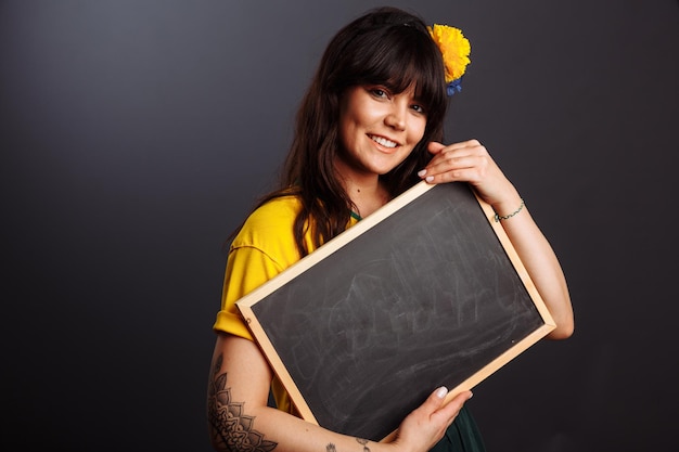 Latin brazil lady in a soccer clothes holding a empty blackboard on his native language isolated on gray background space for text caption