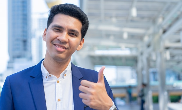 latin businessman show hand gesture thumb up (good sign) at outside city building background