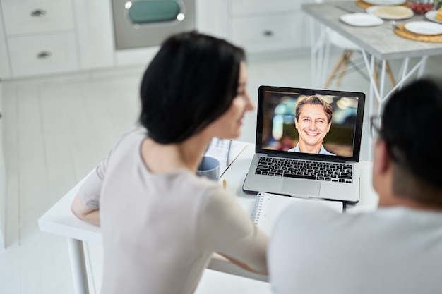 Latin couple making video call using laptop, contacting client by conference, talking on webcam. Online consultation concept. Focus on laptop screen