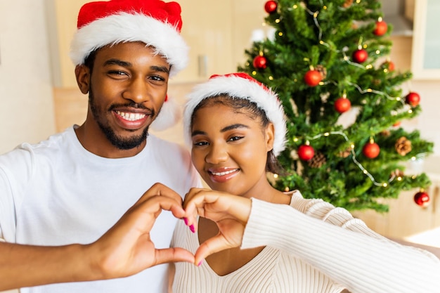 Latin hispanic couple showing heart shape from hands near the christmas tree at home