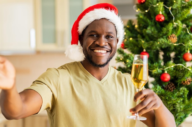 Latin hispanic man in Santa hat talking by video connection with glass of champagne at home