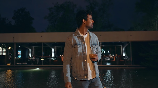 Latin man chilling night walk near water pool relaxed guy holding glass alcohol