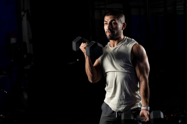 Latin man doing biceps work in the gym with two dumbbells