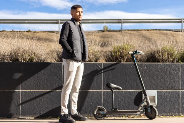 Latin man in formal wear next to an electric scooter on the sidewalk Young latin businessman near an electric scooter