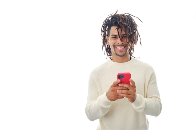 Latin man looking at the camera and smile while holding a mobile phone on an isolated background.